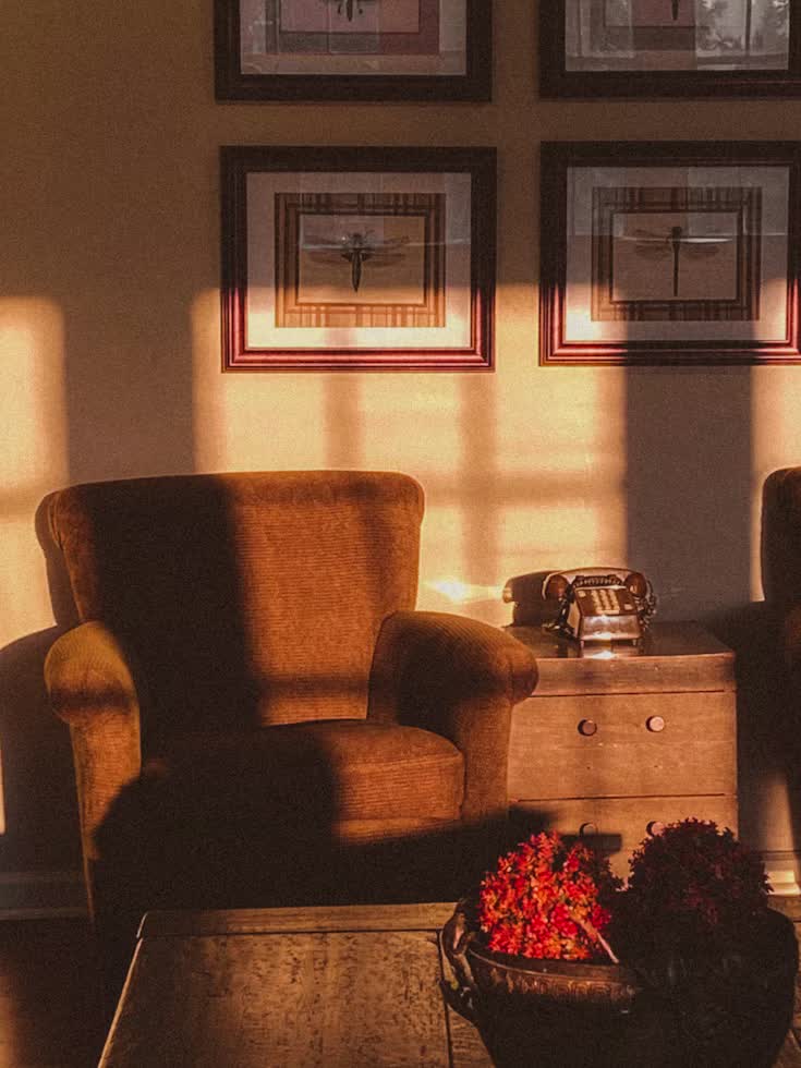 Poltrona acolhedora em tom terracota sob luz quente do fim de tarde, com quadros na parede e flores sobre a mesa