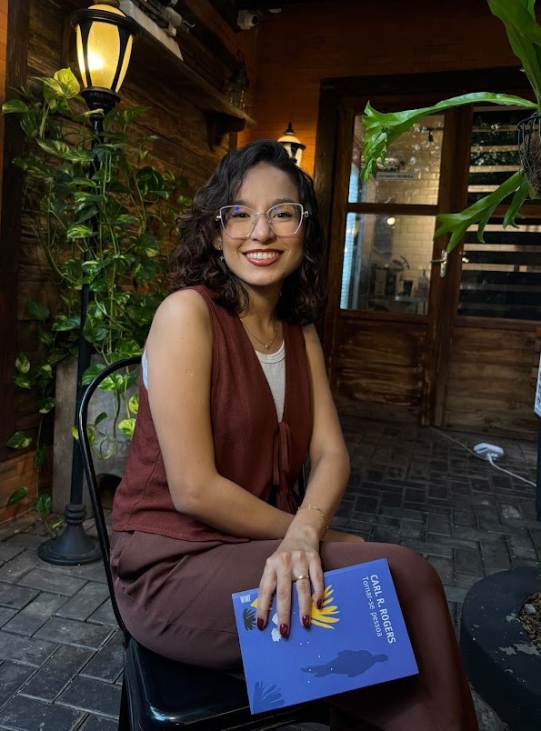 Thafnes Samara sorrindo em ambiente acolhedor com iluminação quente e vegetação